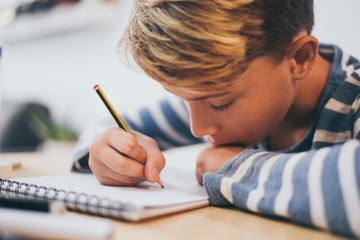 Student drawing with pencil on the notebook. Boy doing homework writing on a paper. Kid hold a...