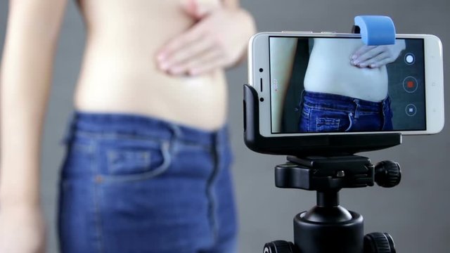 American beauty vlogger applying cream to stomach, creating content for social media vlog, behind phone shot