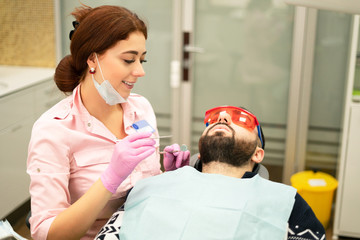 Dentist young woman treats a patient a man. The doctor uses disposable gloves, a mask and a hat. The dentist works in the patient's mouth, uses a professional tool