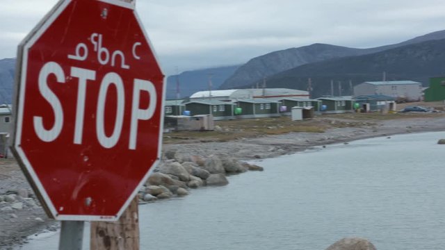 Handheld, close up shot of a stop sign, camera pans to a nearby lake and homes.