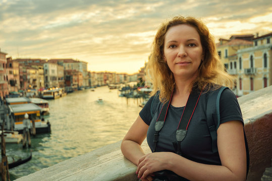 Portrait of young woman on Rialto Bridge at sunset, Venice, Italy. Tourist poses on background of Grand Canal.