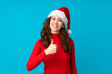 Girl with christmas hat over isolated yellow background giving a thumbs up gesture