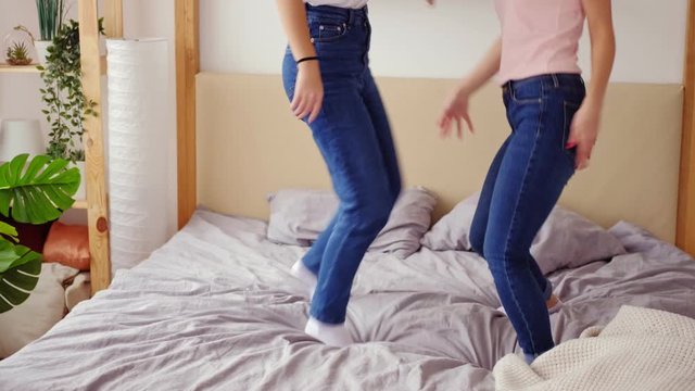 Girls home party. Happiness joy. Two female friends having fun dancing on bed.