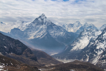 Ama Dablam mountain rises above valley in cloudy day near Cho La pass in Sagarmatha national park in Himalayas. Ghola Tsho lake is visible at the foot  of mountain.