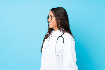 Young doctor woman over isolated blue background looking to the side