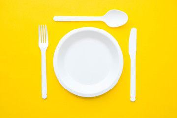Plastic white fork, knife, spoon and plate on yellow background. Cooking utensil. Top view. Minimalist Style. Copy, empty space for text