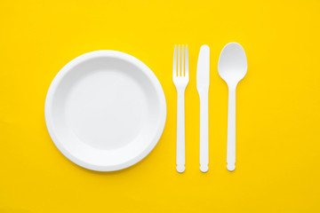 Plastic white fork, knife, spoon and plate on yellow background. Cooking utensil. Top view. Minimalist Style. Copy, empty space for text
