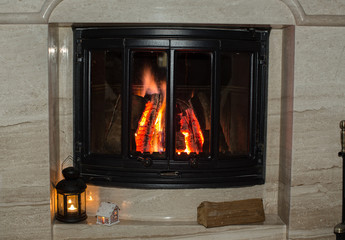 Burning logs in a glass door of a marble fireplace. Lantern with a candle.