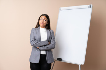 Young woman giving a presentation on white board making doubts gesture while lifting the shoulders