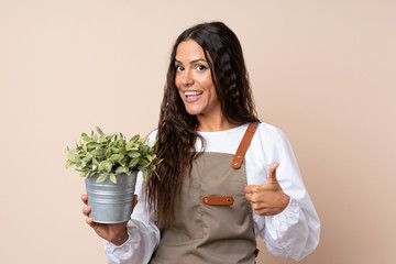 Young woman holding a plant with thumbs up because something good has happened