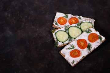 Crispbread with curd cheese, cherry tomato and cucumber, on a dark background. Space for text. Flat lay, top view. Diet snack.