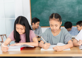 pretty asian students group do homework in classroom, they sharing knowledge together, they explaining about important lesson to friends, happiness elementary school