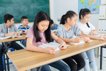 pretty asian students group do homework in classroom, they sharing knowledge together, they explaining about important lesson to friends, happiness elementary school