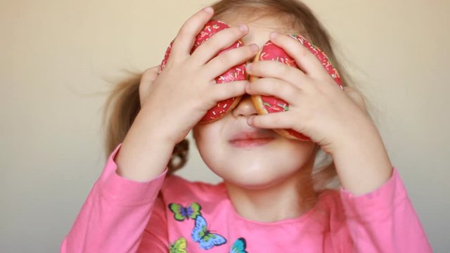 Child eats donut. Closeup baby girl eating doughnut with glase. Delicious, sweet, sweettooth