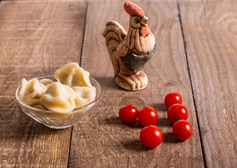 Clay figure of a rooster, dumplings and cherry tomatoes on a wooden table.