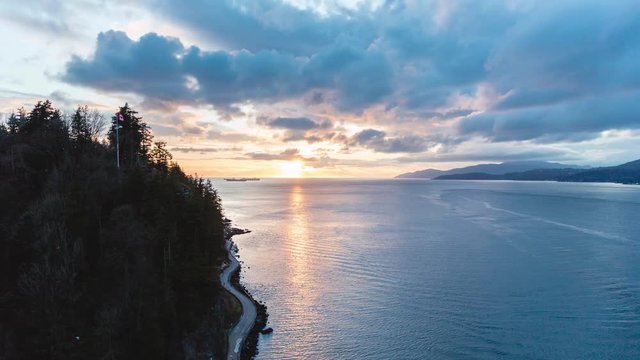 Time lapse of a Prospect Point in Stanley Park during incredibly colorful sunset. People casually walking down picturesque seawall, a tug boat passing by while sun is showing through cumulus clouds