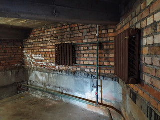 Basement of a residential building. The walls are made of red clay brick. In the basement are engineering networks. The basement is heated, the heating elements are cast iron radiators.