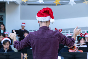 Back view of a male conductor, wearing casual outfit with red santa hat, conducting his young band...