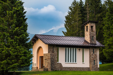 Fototapeta na wymiar Christian church on a meadow near forest with mountains behind it.