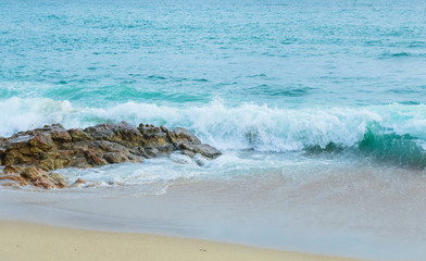 The waves, turquoise in color, splash and break on the rocky rock on the shore, with spray and foam