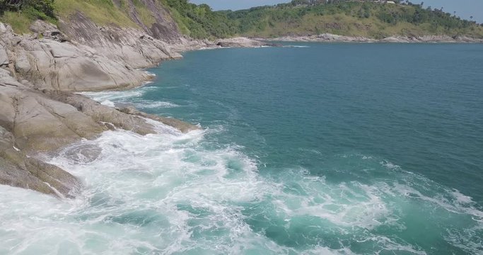 Sea coastline view, rock on the shore with blue sea water ripple swash on there in sunny day with mountain behind, hold still footage background from drone in 4K