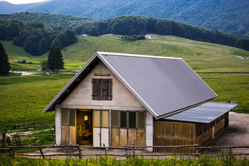 Fototapeta na wymiar Rural building with stables inside with meadow, forests and hills in the background.