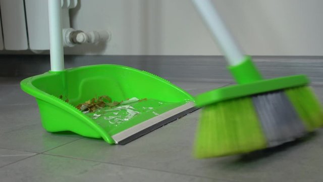 Household broom sweeping dirt on green plastic dustpan, house hygiene, cleaning