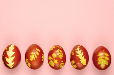 Easter decorated eggs on pink background. Five eggs dyed with onion peels with a pattern of fresh leaves in a row. Minimal Easter concept. Happy Easter card. Copy space for text. Top view, flat lay