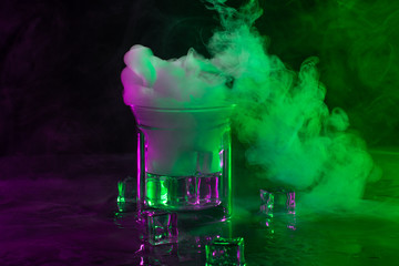 A glass with ice cubes in colourful smoke