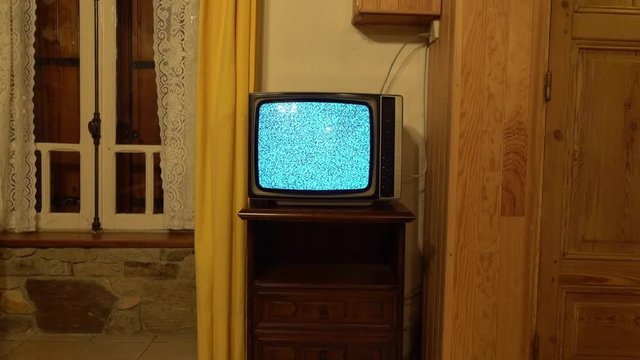 Old black and white TV with no signal just noise in a rustic setting. Real shoot in a stone rustic house with a wooden door and yellow curtains on the window with closed shutters.
