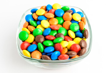 Group of small mixed red, green, yellow, orange, brown and blue coated chocolate candies in a squared bowl isolated on white background, top view or flat lay