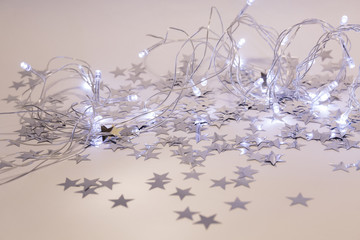 Christmas garland with glowing lights on a white background with scattered silver stars