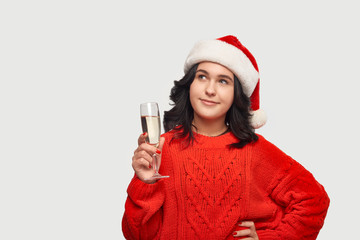 Beautiful brunette girl in a red sweater and Santa hat holding glass of champagne.