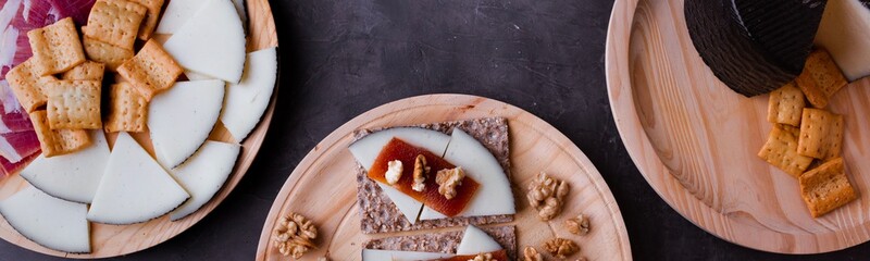 Variety of wood plates with freshly jamon, cheese and roasted bread; a whole cheese and toasted bread with cheese, nuts and quince jelly.