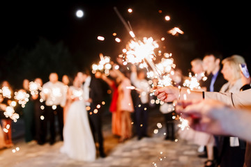 A crowd of young happy people with sparklers in their hands during celebration. Sparkler in hands on a wedding - bride, groom and guests holding lights in hand. Sparkling lights of bengal fires.