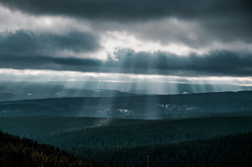 Dramatic nature winter weather sky with clouds and sun light rays and wide panorama mountain view. Brocken, Harz National Park Mountains in Germany