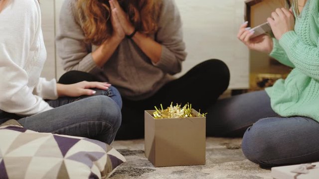 Winter holiday surprise. Fun congratulation. Teen girls sitting on floor at home opening gift.