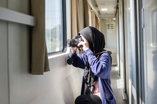 Young muslim female traveller wearing hijab taking a photo from inside a train.
