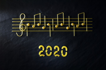 Musical Italian pasta 2020 in the form of notes, isolated on a black textural background.