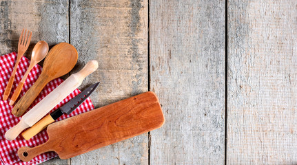 Kitchen utensil tools including cutting board, knife and spoons with rustic wooden background. Top view.