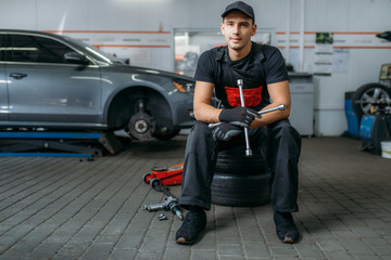 Auto mechanic sitting on wheels, tire service