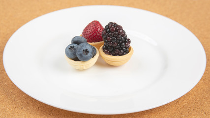 Blackberry, blueberry and strawberry in a waffle basket on a white plate. Vitamins and wholesome foods