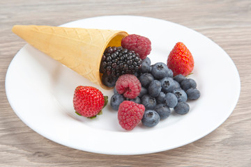 Different fresh berries in a waffle glass on a white plate. Vitamin and healthy food.