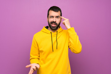 Handsome man with yellow sweatshirt making the gesture of madness putting finger on the head