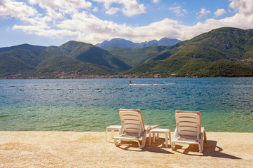 Fototapeta na wymiar Summer vacation. Beautiful sunny landscape with two chaise lounges on beach. Montenegro, Adriatic Sea, view of Bay of Kotor near Tivat city