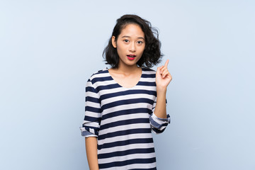 Asian young woman over isolated blue background thinking an idea pointing the finger up