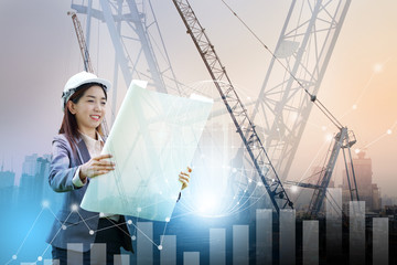 Female engineer wearing a white hat holding a blueprint The backdrop is modern machines, built tall buildings and urban communities and has graphics showing growth. Urban development concept