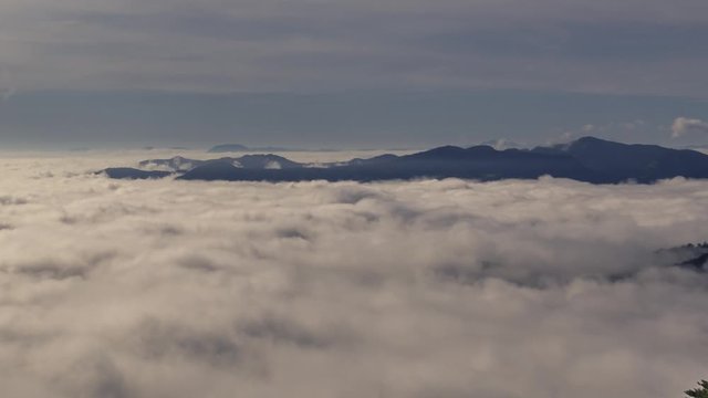 Time lapse rolling inversion clouds in valley with contrail shadow and hilltops in background
