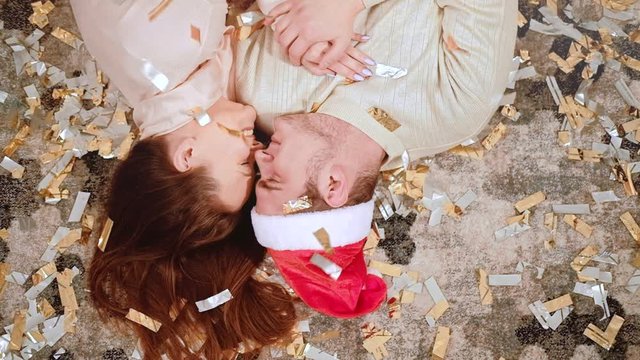 Romantic Christmas. Love affection. Happy couple lying down on floor in confetti rain smiling.