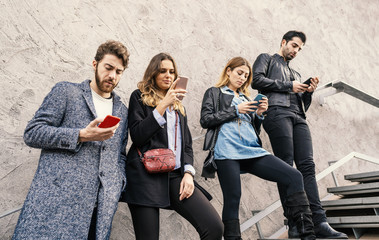 Millennials generation smartphone addiction concept. Group of people using smartphones against a concrete wall in the upstairs.